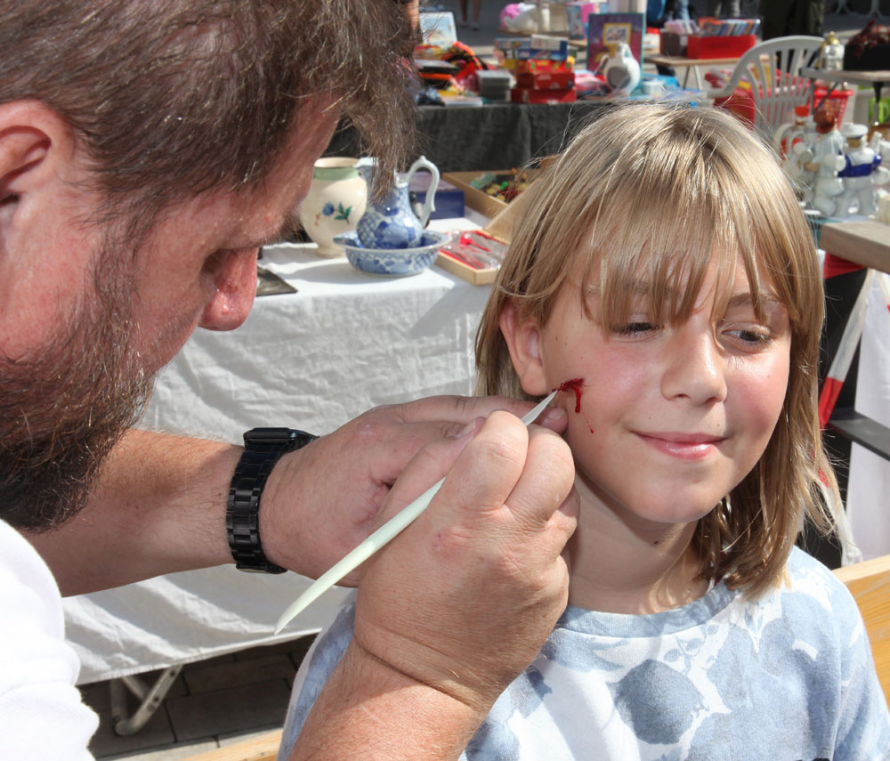 Rotkreuz-Mitarbeiter Günther Schleelein schminkt einem Mädchen eine Verletzung ins Gesicht. (Foto: Michael Will / BRK)