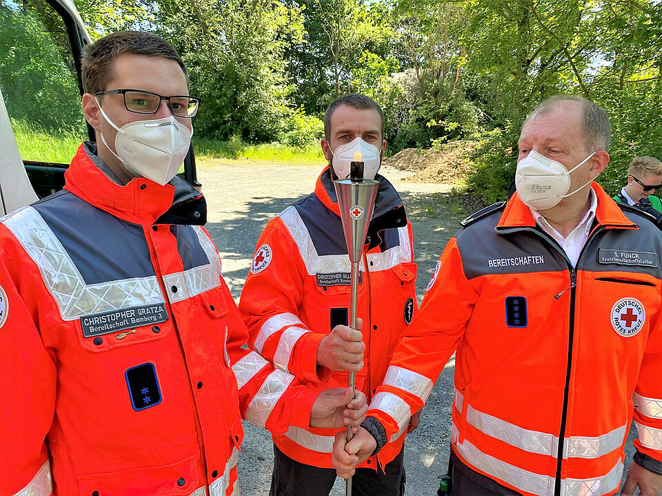 Ein ganz besonderer Moment: Stefan Funck (rechts), BRK-Kreisbereitschaftsleiter aus den Haßbergen, übergibt die Fackel an die Kollegen aus dem Kreisverband Bamberg. Christopher Gratza (links) und Christopher Gillitzer (Mitte) machten sich damit anschließend auf den Weg durch Oberfranken. (Foto: Michael Will / BRK)