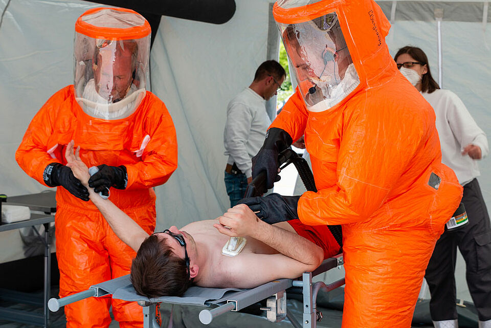 Mitglieder einer CBRN(E)-Einheit in Gebläseschutzanzügen dekontaminieren einen Verletzten, der zuvor bei einem Unfall in einem Unternehmen mit einer Chemikalie in Kontakt gekommen ist. (Foto: Jonas Pröschel / BRK) 