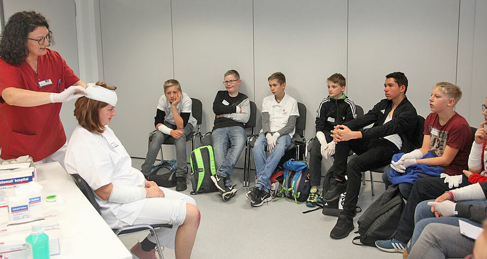 Gespannt verfolgen die Schüler, wie Krankenschwester Manuela Hörhager bei ihrer Kollegin Eva Hückmann einen Kopfverband anlegt. (Foto: Michael Will / BRK)