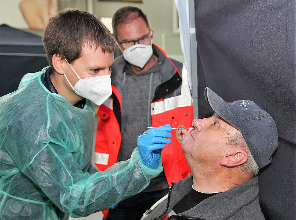 Der Nasenabstrich für den Schnelltest, den Christian Latzo (links) bei Herbert Gehrig aus Prappach durchführt, dauert nur wenige Sekunden. Wolfgang Zweverink (Mitte), zuständiger Organisator beim BRK für die Testzentren, schaut beiden dabei in der Haßfurter Eishalle über die Schulter. (Foto: Michael Will / BRK)